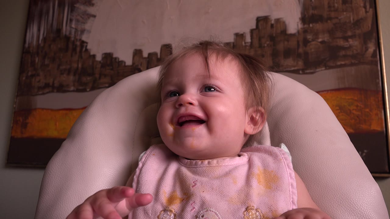 Smiling toddler facing more toward the camera in a chair.