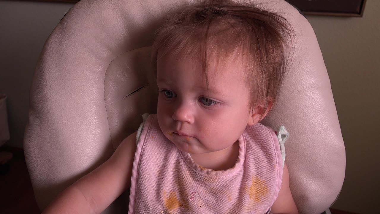 Child in a pink top sitting close to camera in a cream chair.