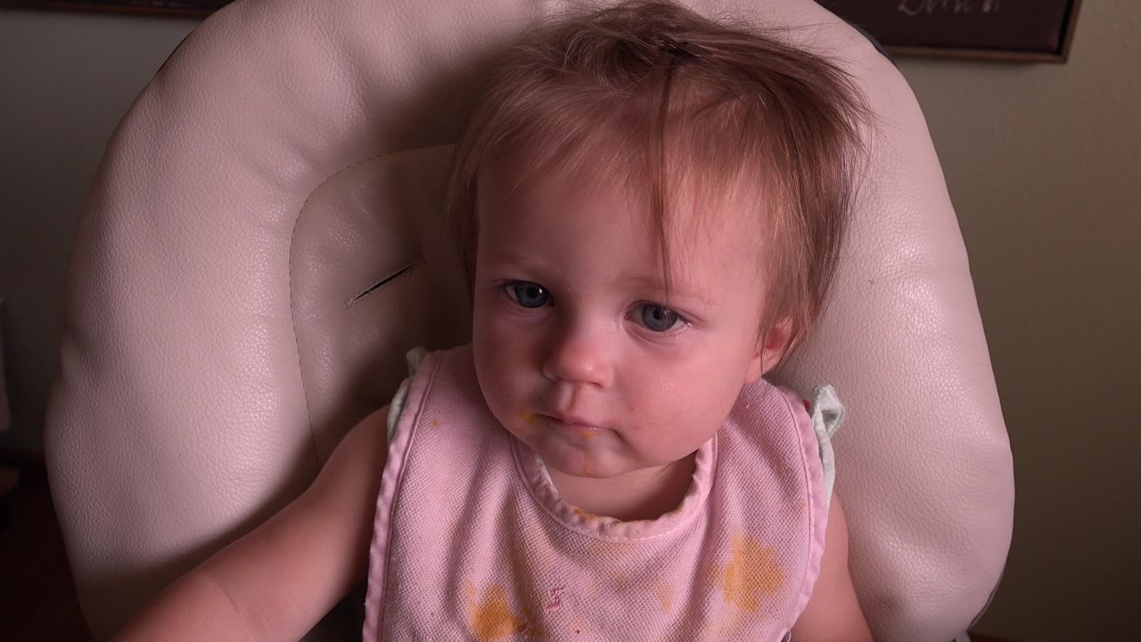 A baby girl with blue eyes looks toward the camera from a pale padded chair in the Hidden Lake, Colorado clip.