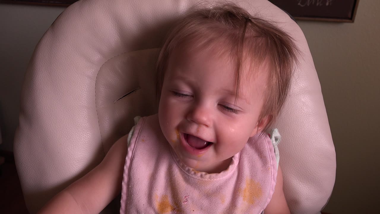 Baby girl laughing with eyes partly closed.