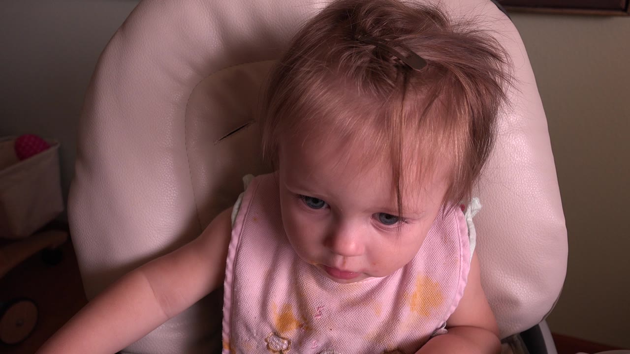 At 0:00, a blond baby in Hidden Lake, Colorado sits in a pale padded highchair, looking slightly downward with a pink bib visible.