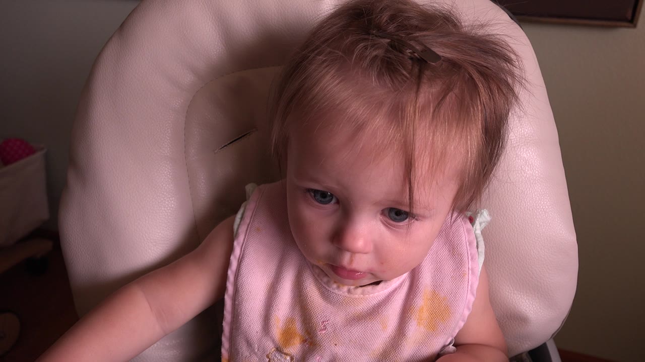 At 0:02, the baby in Hidden Lake, Colorado faces more toward the camera, with blue eyes visible and the pink bib catching the soft indoor light.