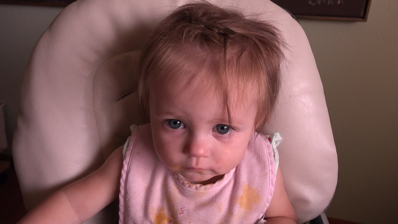 Baby seated in a highchair looking directly toward the camera.