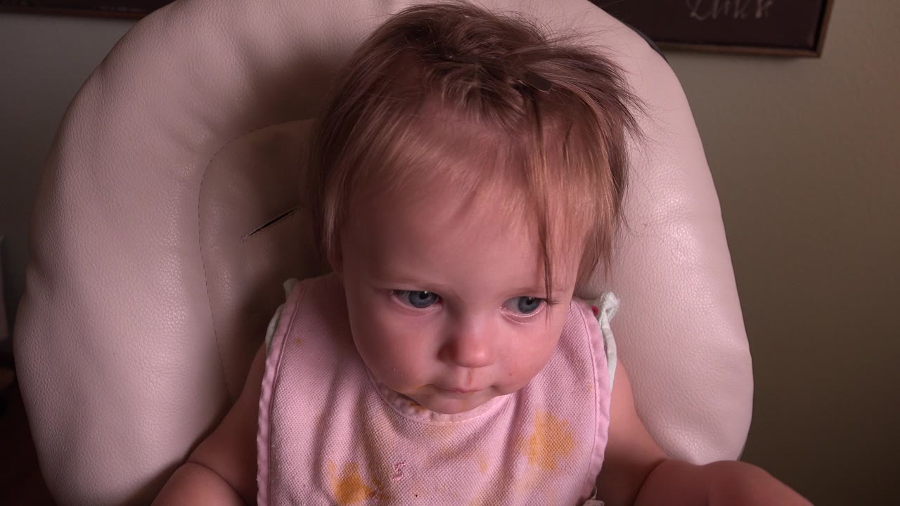Baby in pink clothing seated in a padded chair.