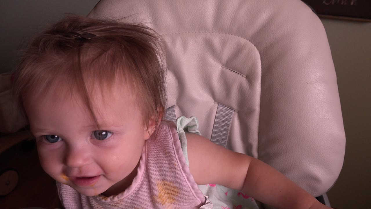 Baby in a pale feeding chair looking up at the camera.