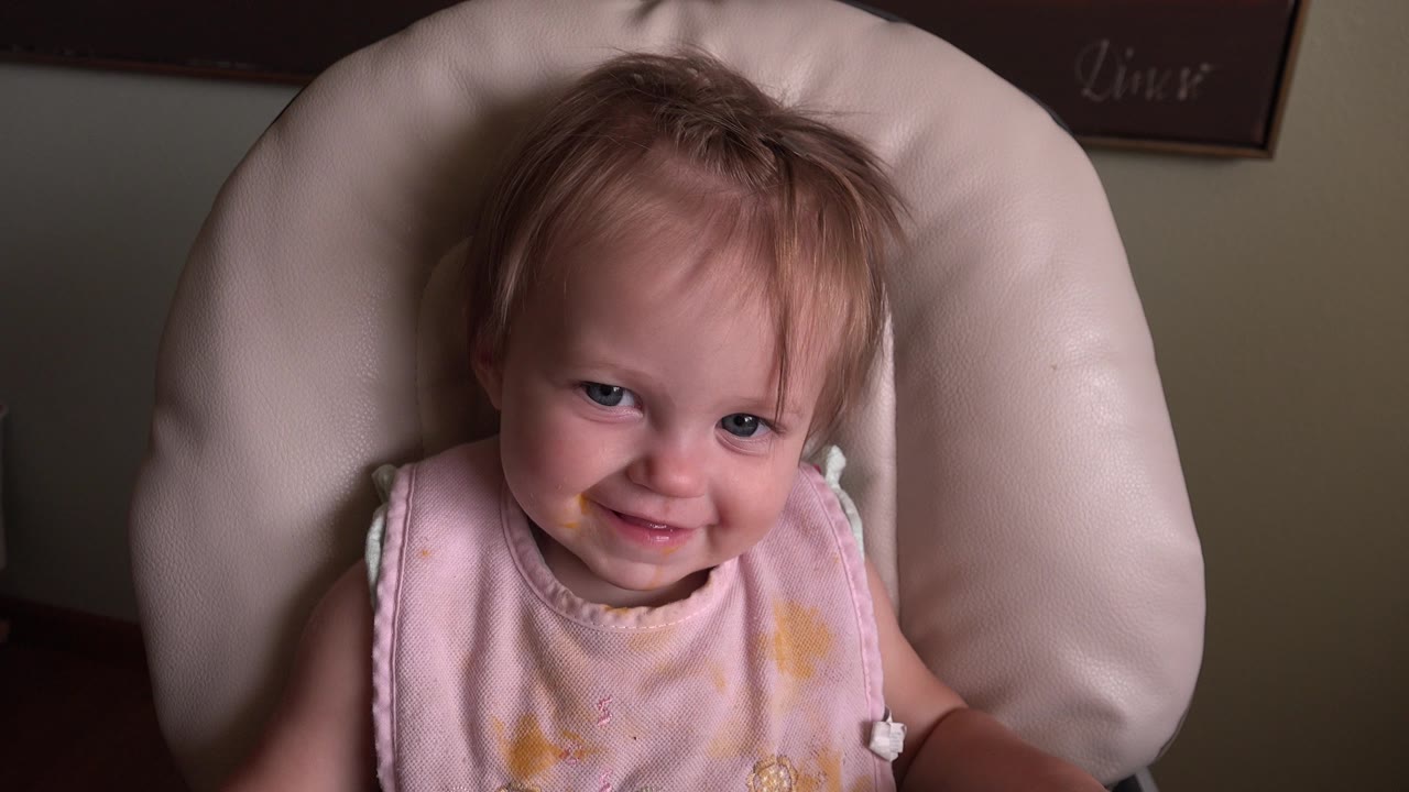 Baby in a pink bib sitting in a padded highchair.