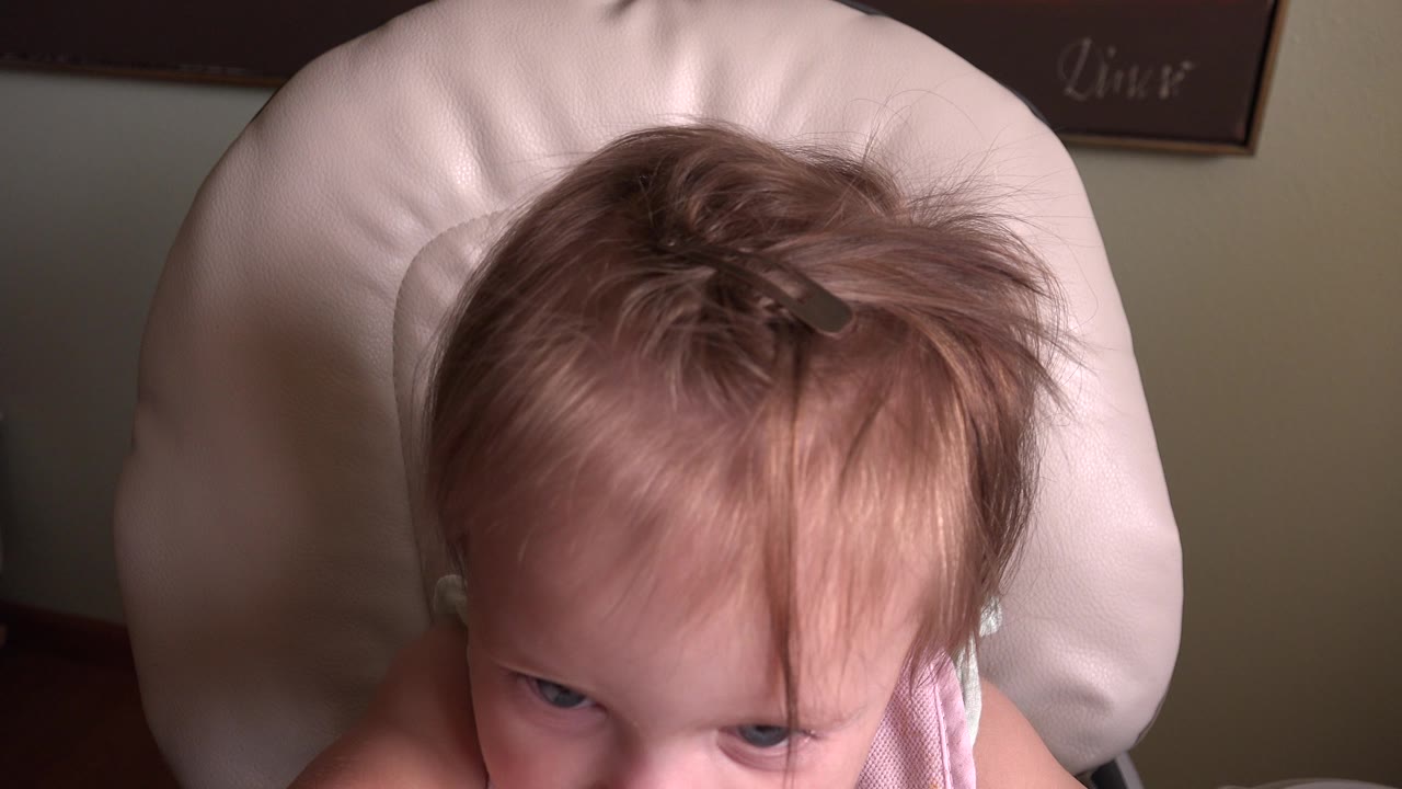 At 0:01 in Hidden Lake, Colorado, the toddler remains centered in the high chair, eyes visible below wispy hair and a small clip near the crown.