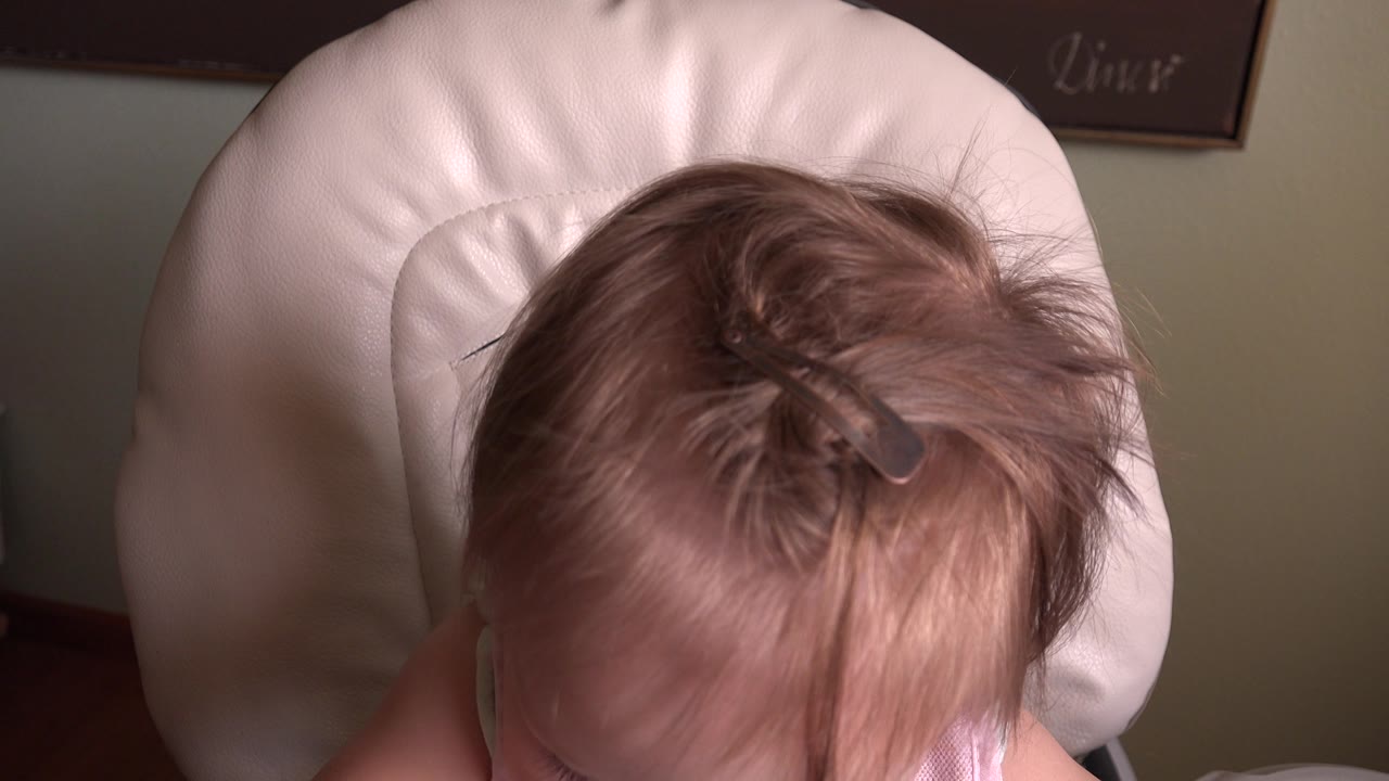 Top of toddler's head with hair clip as the child looks downward.