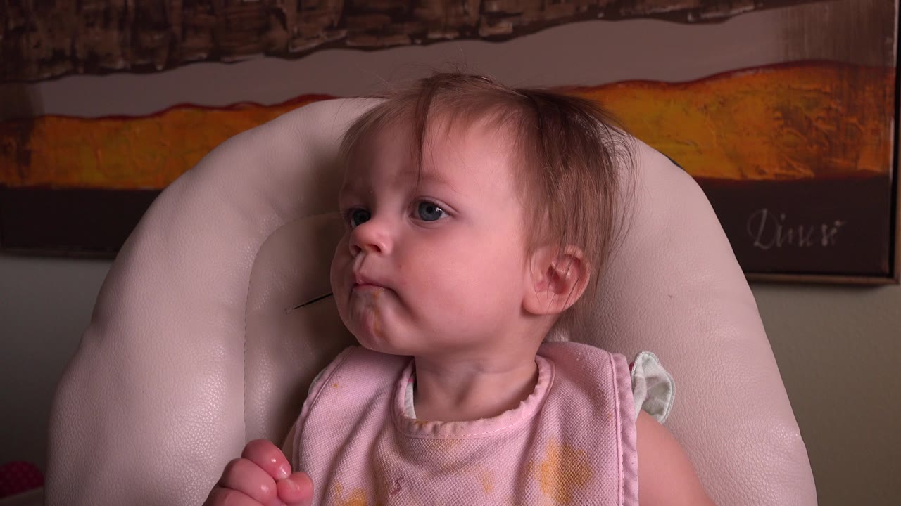 Baby seated in a pale cushioned chair looking left