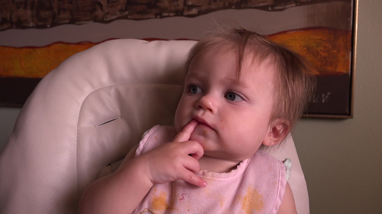 Toddler in a high chair sucking an index finger.