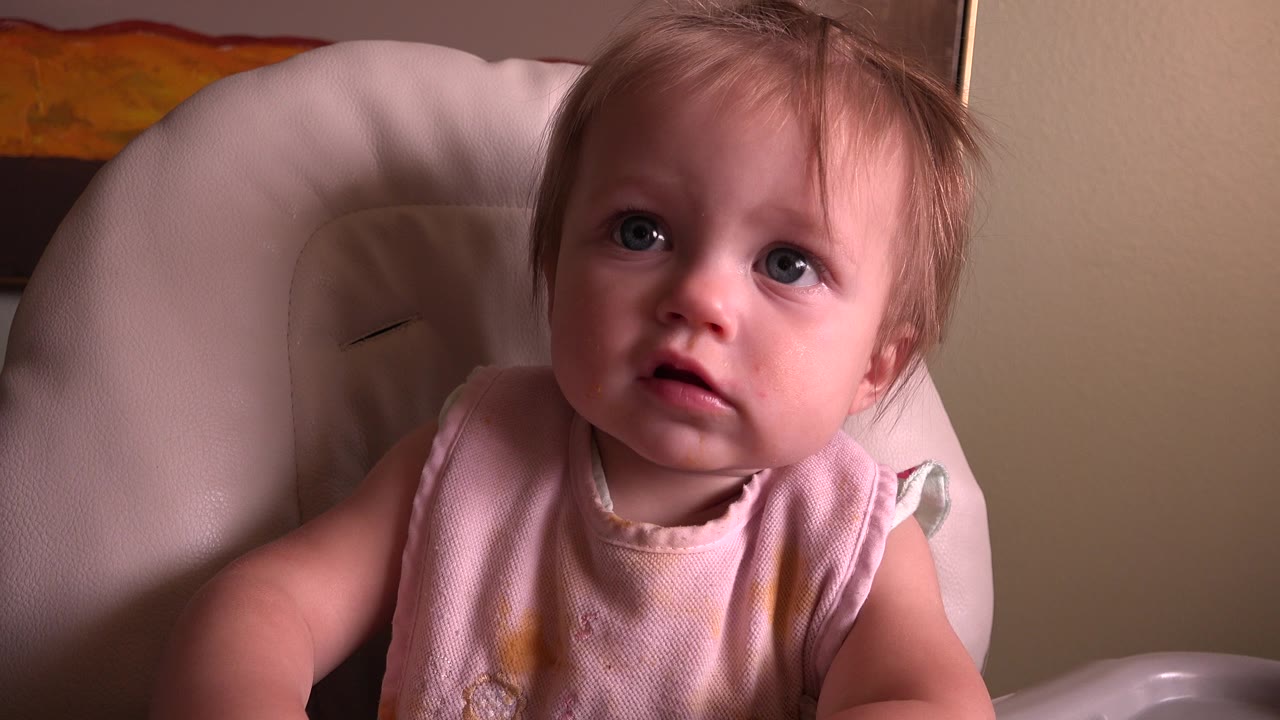 Young girl in a pale highchair looking upward.