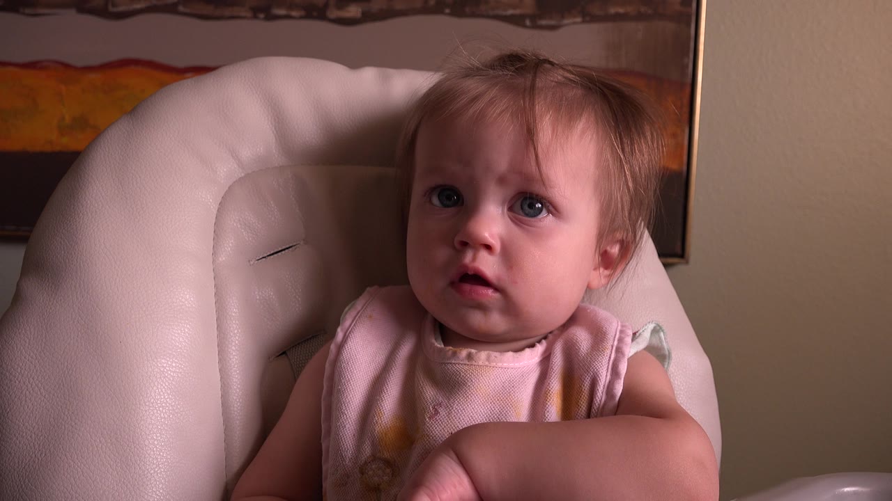 Young child in a pale padded chair looking toward the camera.