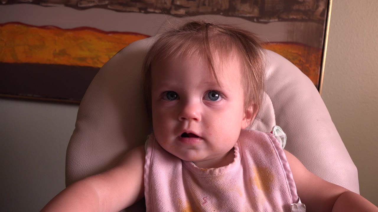 Baby with blue eyes seated in a padded chair.
