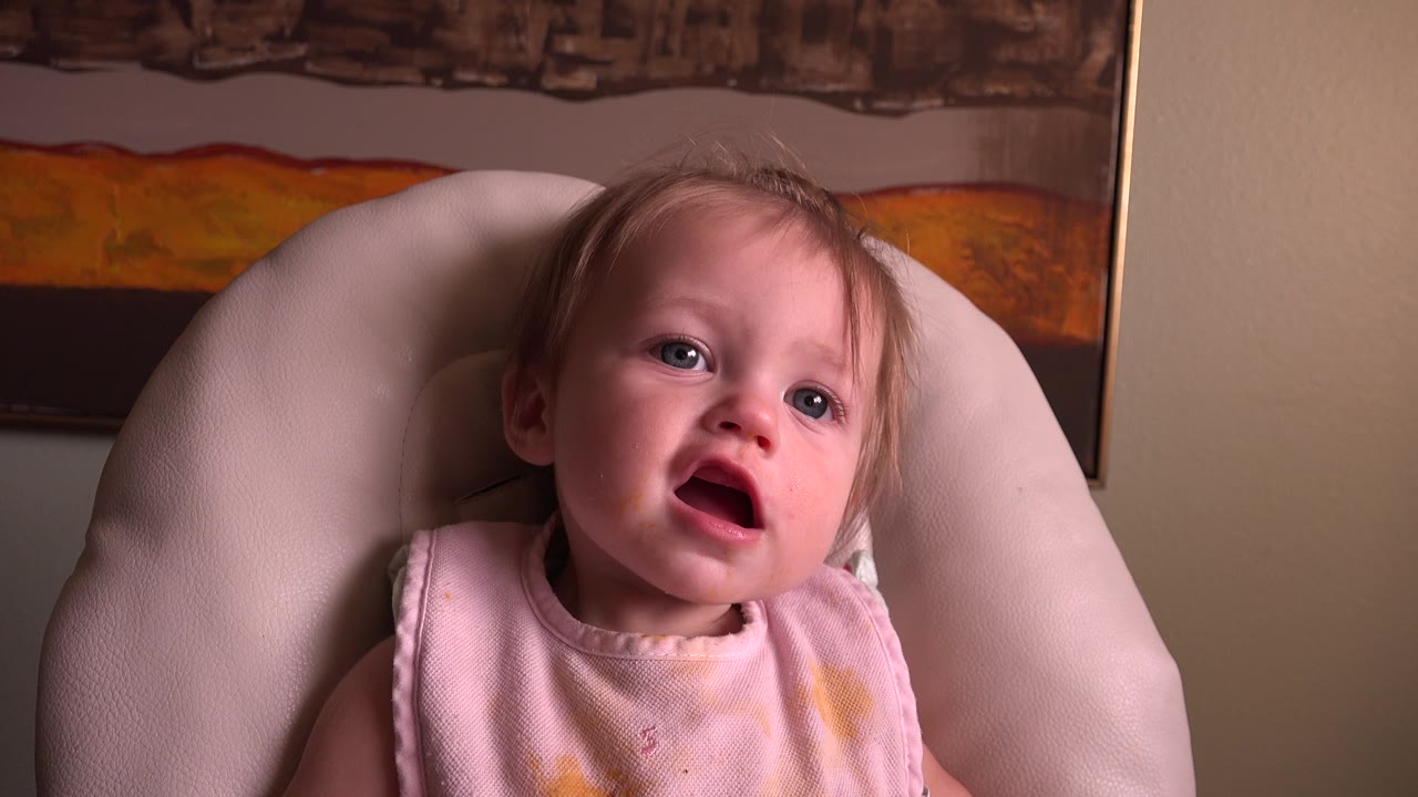 At 0:01, the baby looks slightly upward from the cushioned feeding chair in Hidden Lake, Colorado, with the same framed artwork filling the background.