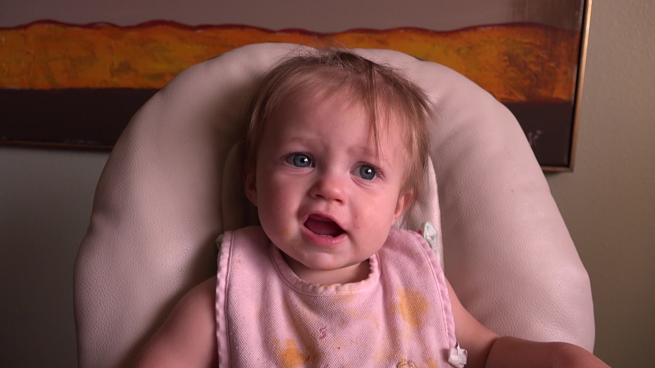 At 0:00, a baby sits in a pale pink cushioned chair in Hidden Lake, Colorado, looking slightly upward with a framed artwork on the wall behind.