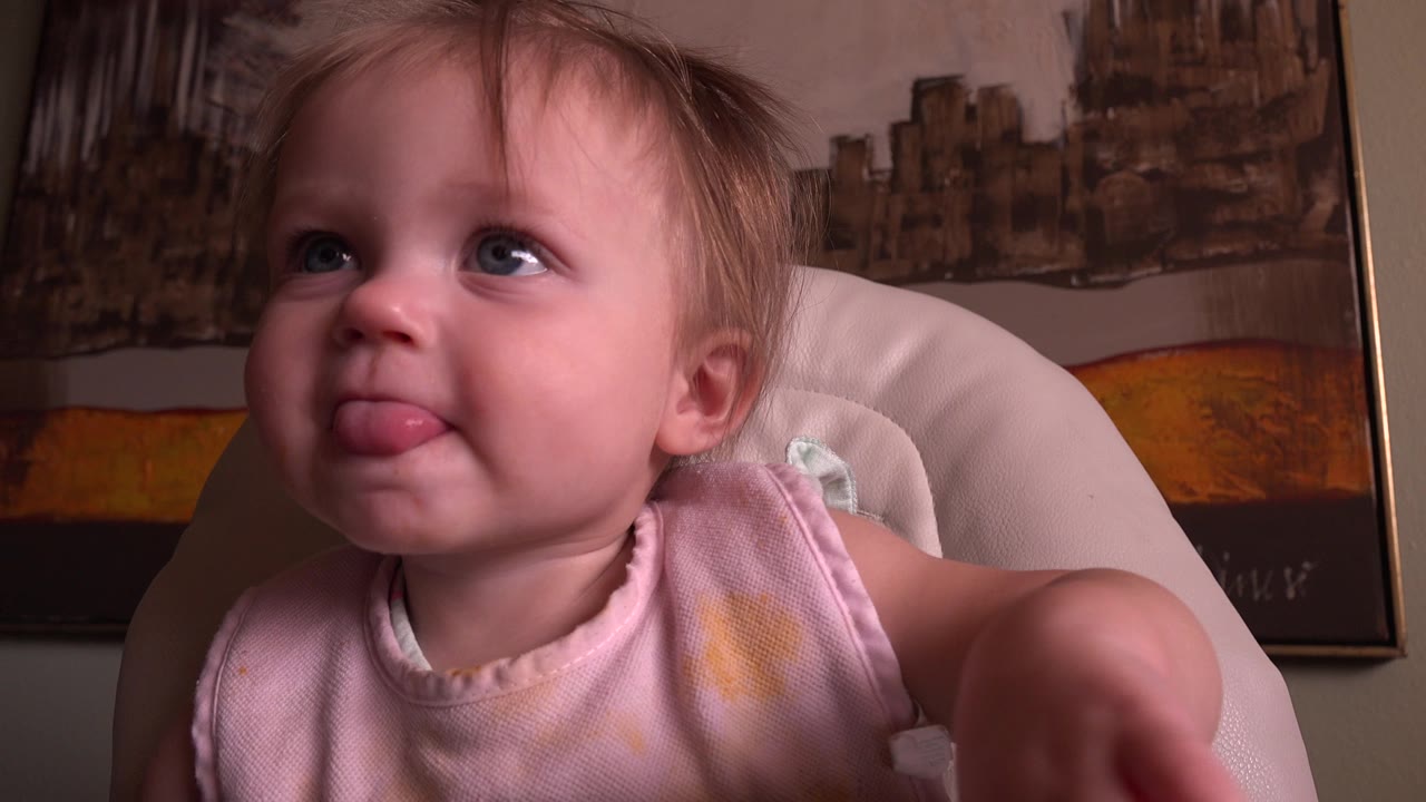 At 0:00 in the Hidden Lake, Colorado 2015 clip, a baby sits close to the camera in a pale chair, looking up to the left with their tongue out and framed wall artwork behind them.