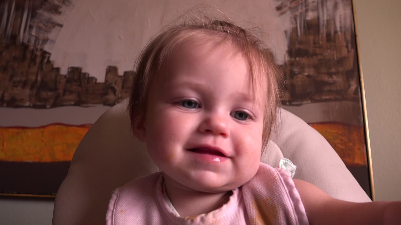 Baby smiling in a light chair with framed artwork behind.
