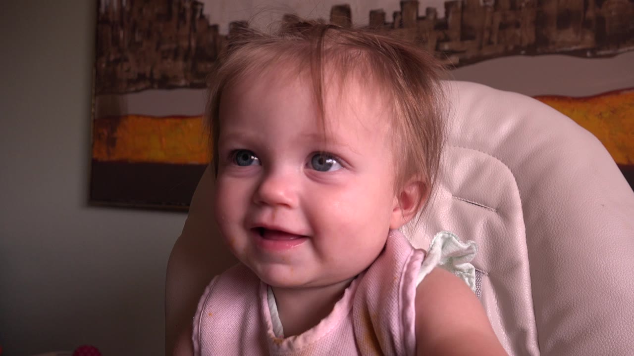 The baby keeps smiling and looks slightly upward from the white high chair, with the Hidden Lake, Colorado clip retaining the same warm interior background.