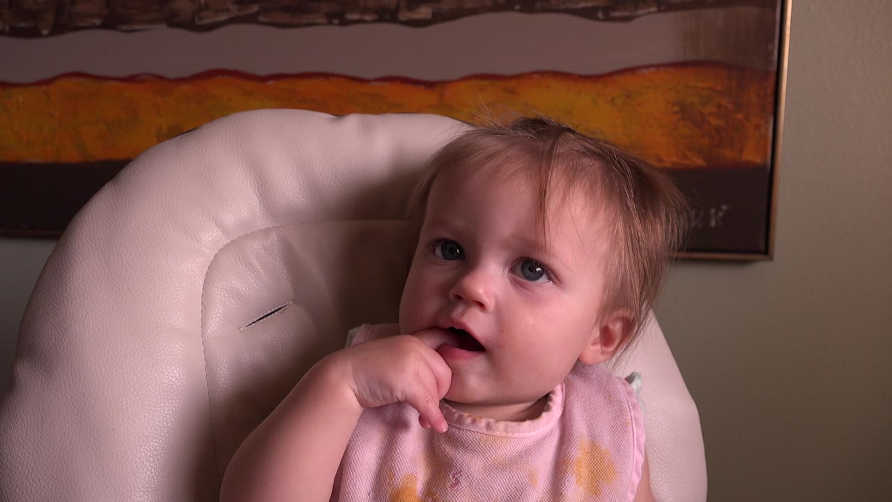 Young child in a high chair with fingers near mouth.