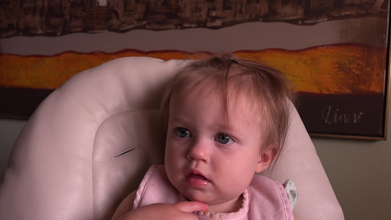 At 0:01, the baby remains centered in the high chair, her hand near her chin and her eyes turned slightly to one side inside the Hidden Lake, Colorado home.