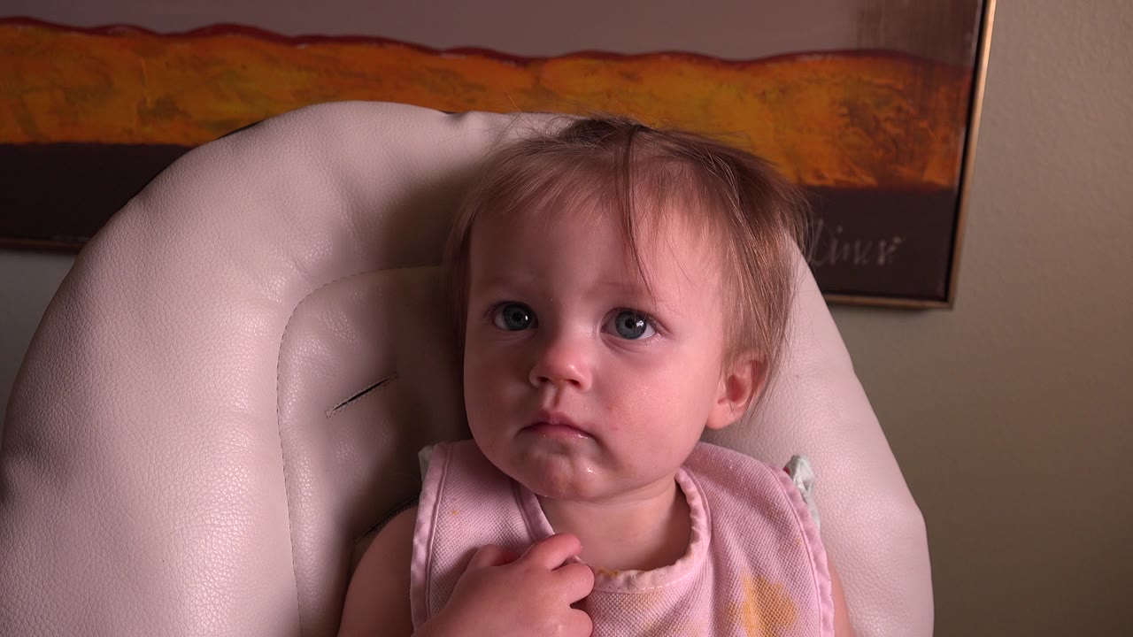 Young girl in bib faces forward in a padded chair.