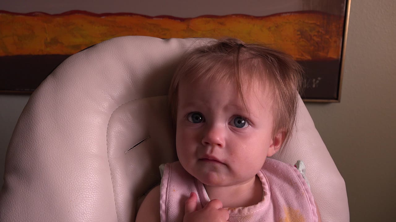 Young child in a pink bib seated in a pale armchair.