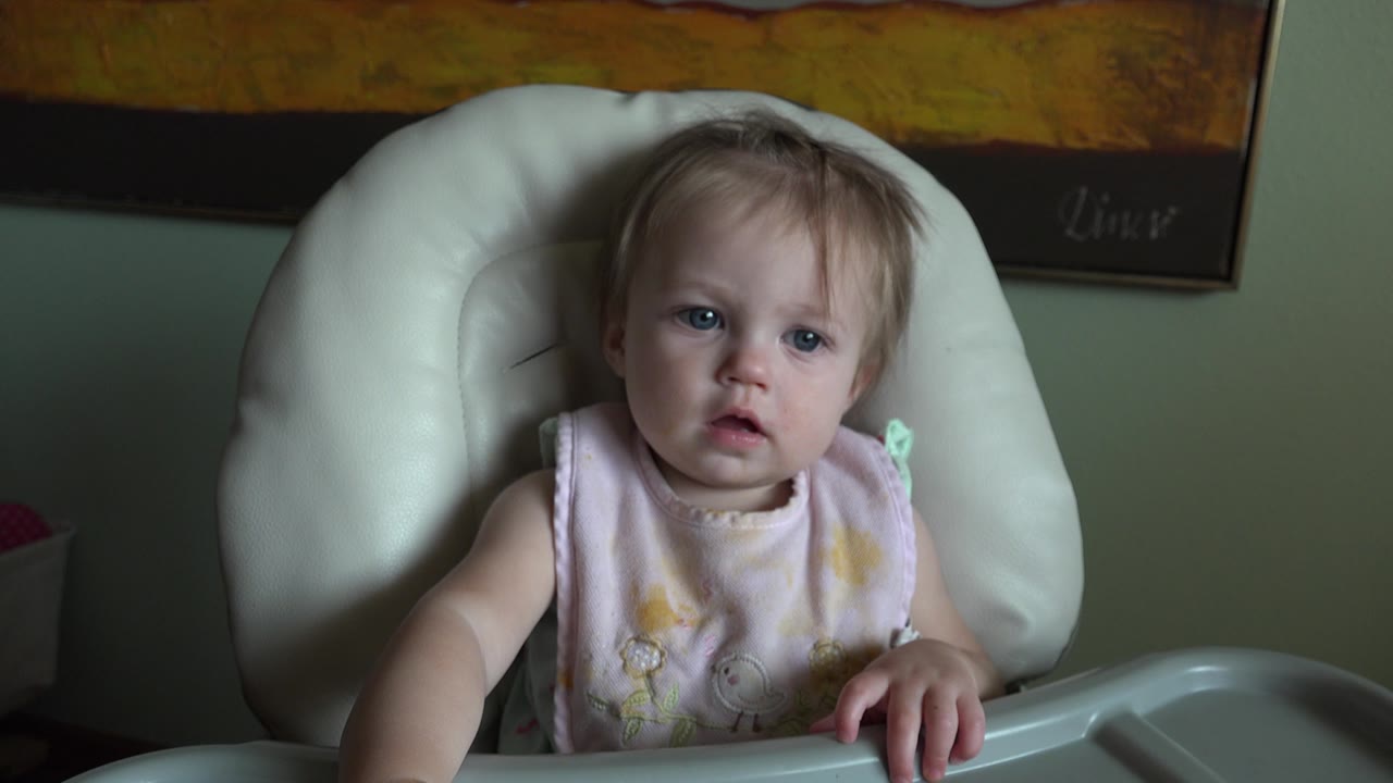 At 0:01, the baby remains centered in the high chair in Hidden Lake, Colorado, with one hand resting on the tray and eyes turned slightly forward.