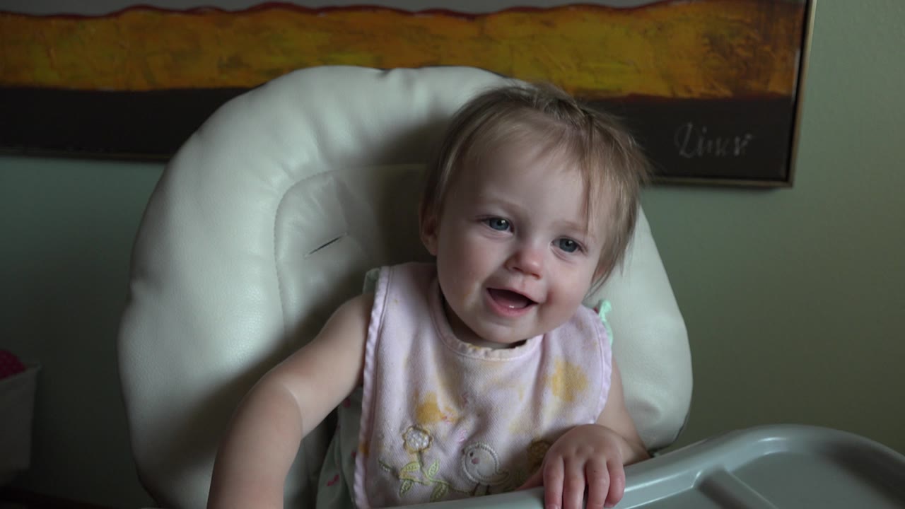 Young child smiling in a white high chair.