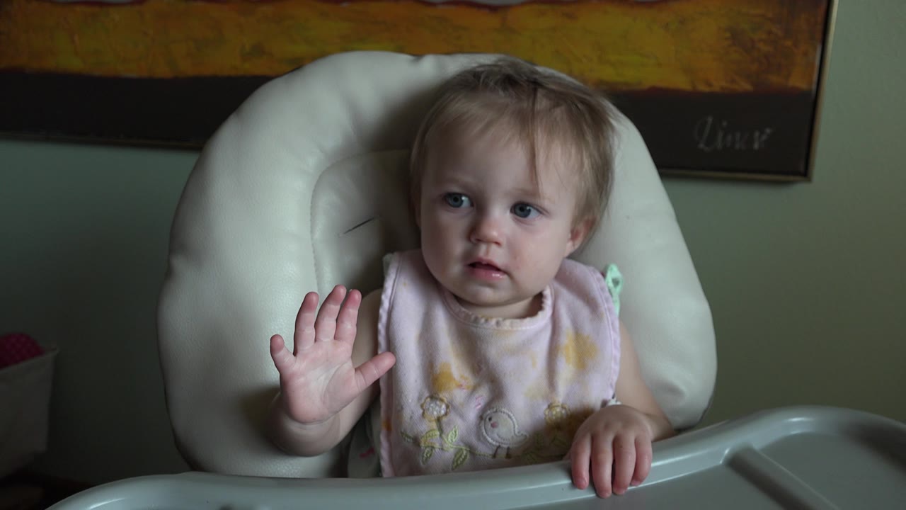 The child remains seated in the highchair, looking forward with the left hand lifted and the right hand resting on the tray inside the Colorado home setting.