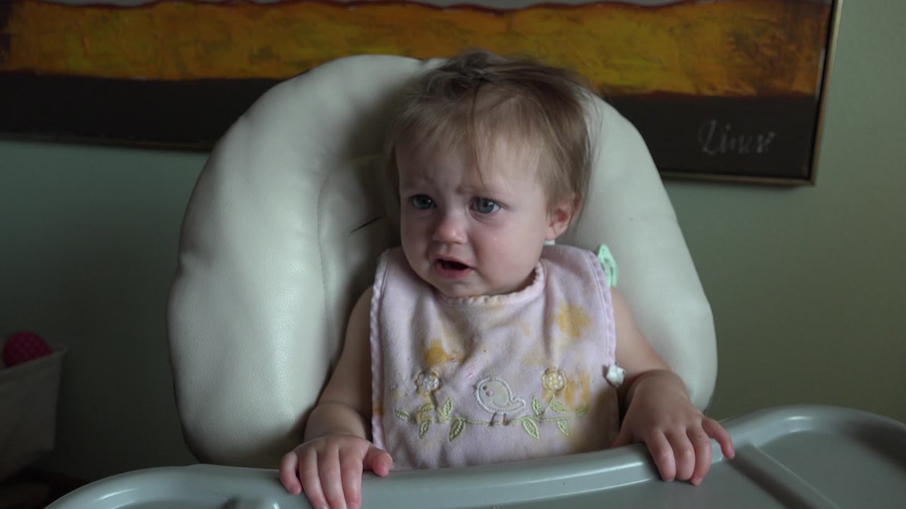 Young girl in high chair with mouth open.