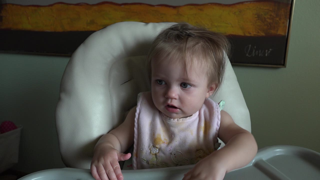 Blond baby sitting in a high chair and looking left.