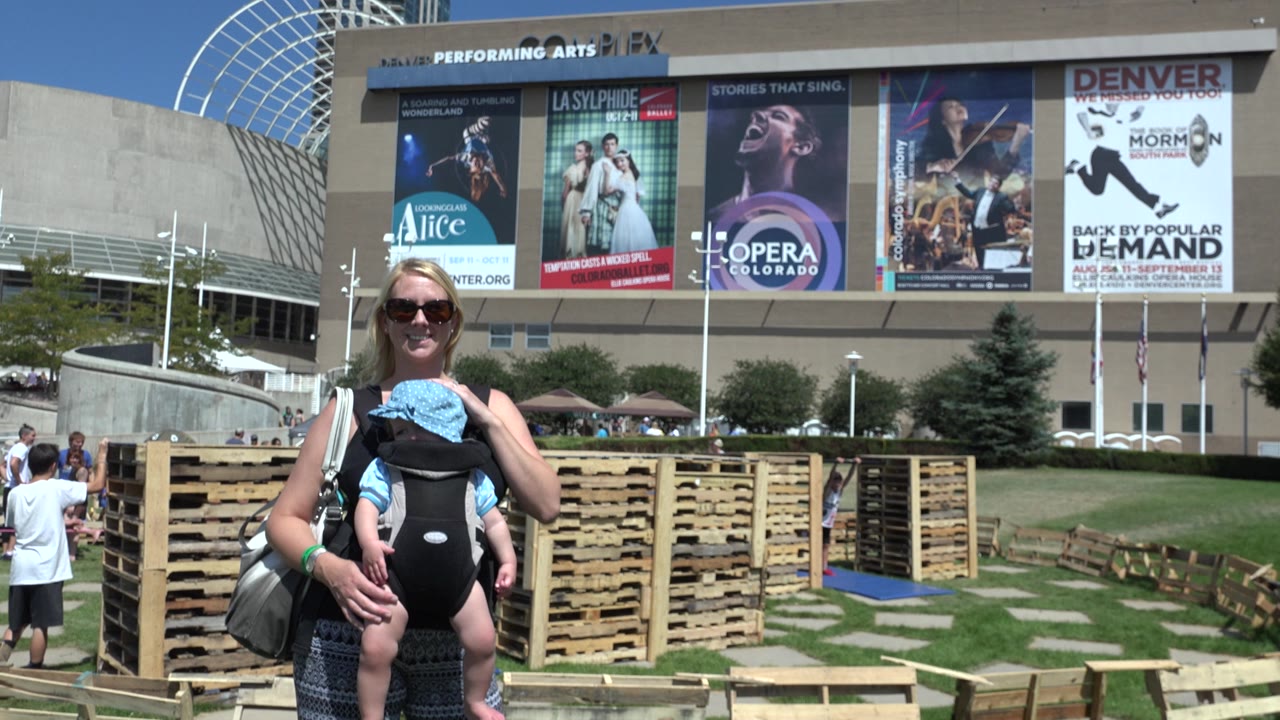 Woman with baby stands near wood pallets and venue posters.