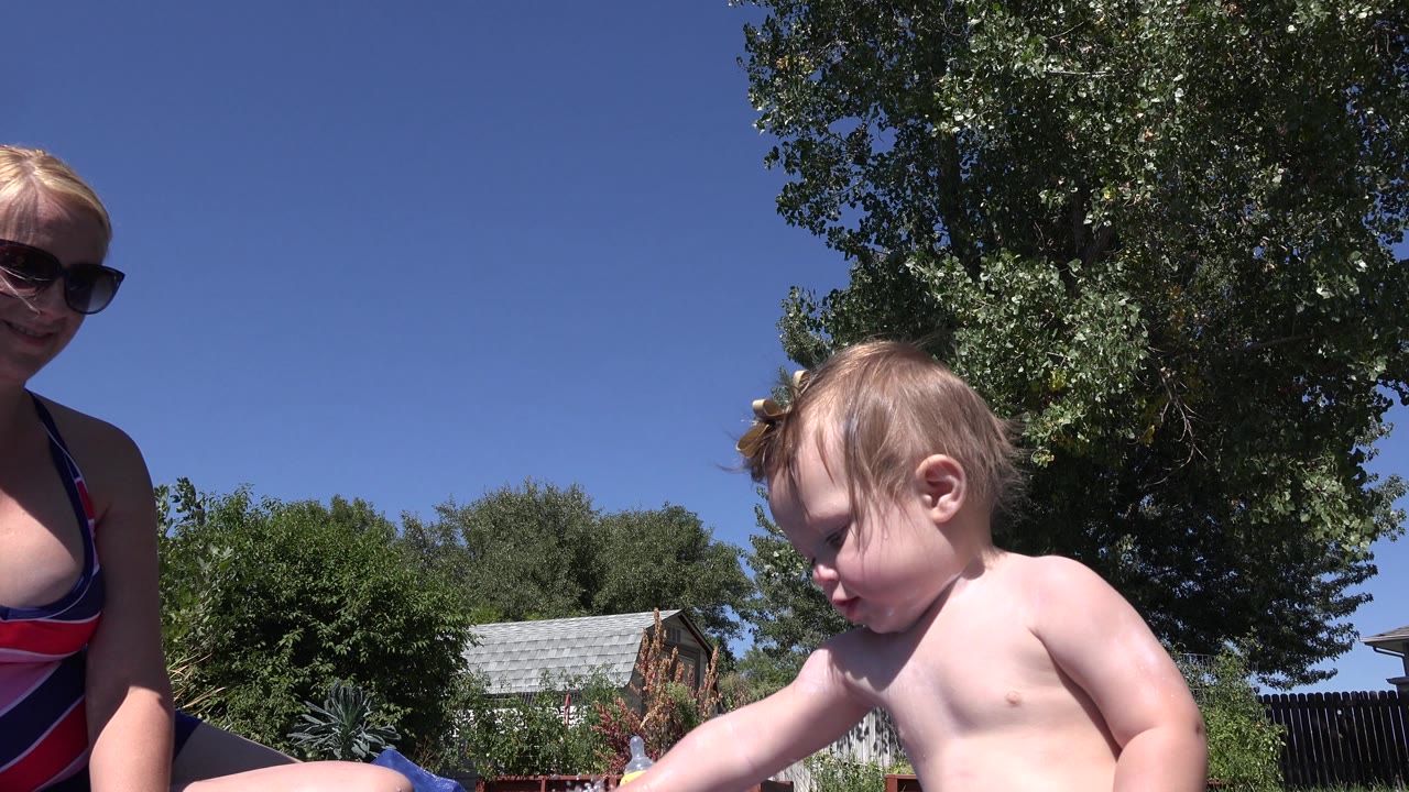Baby facing down near bottles and a hose on a blue mat in the yard.