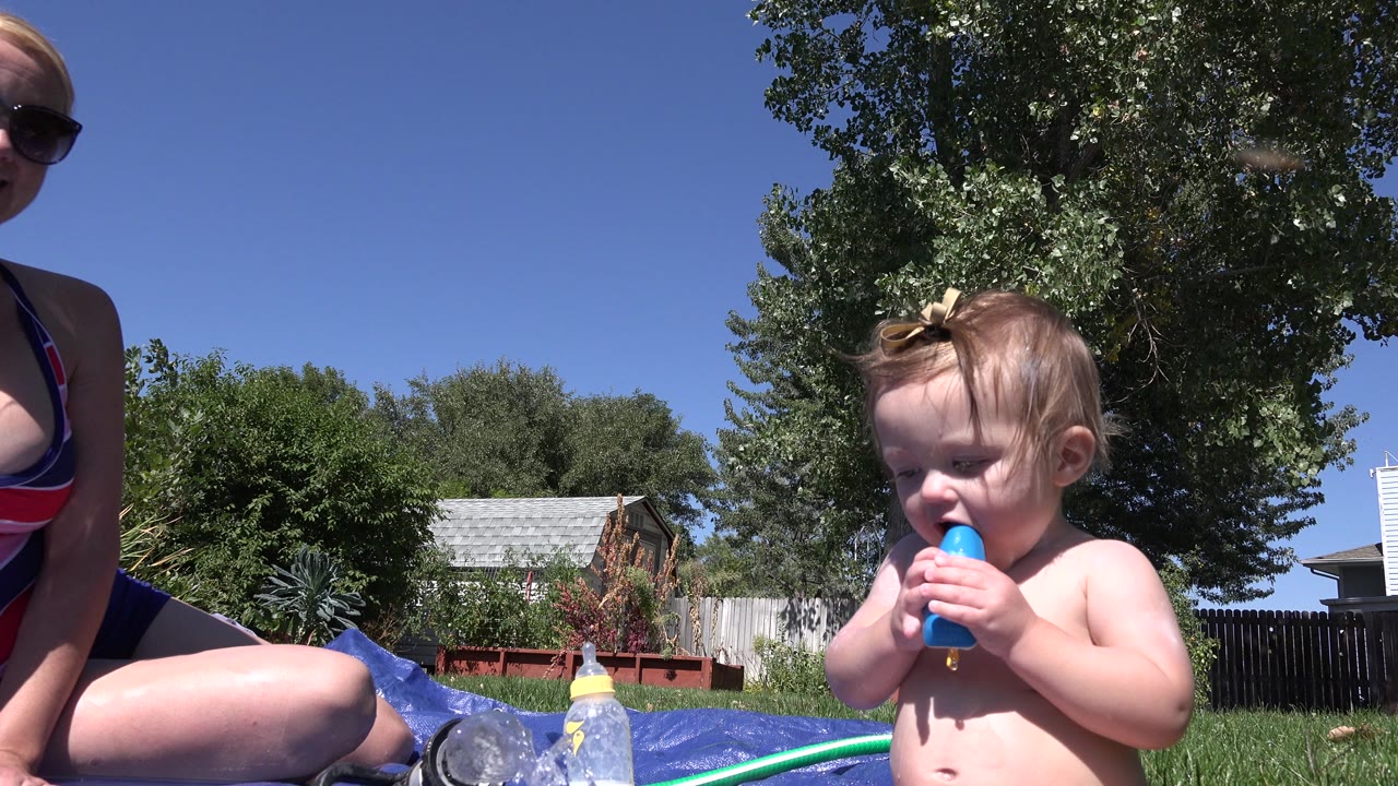 Baby holding a blue treat beside a partially visible adult outdoors.