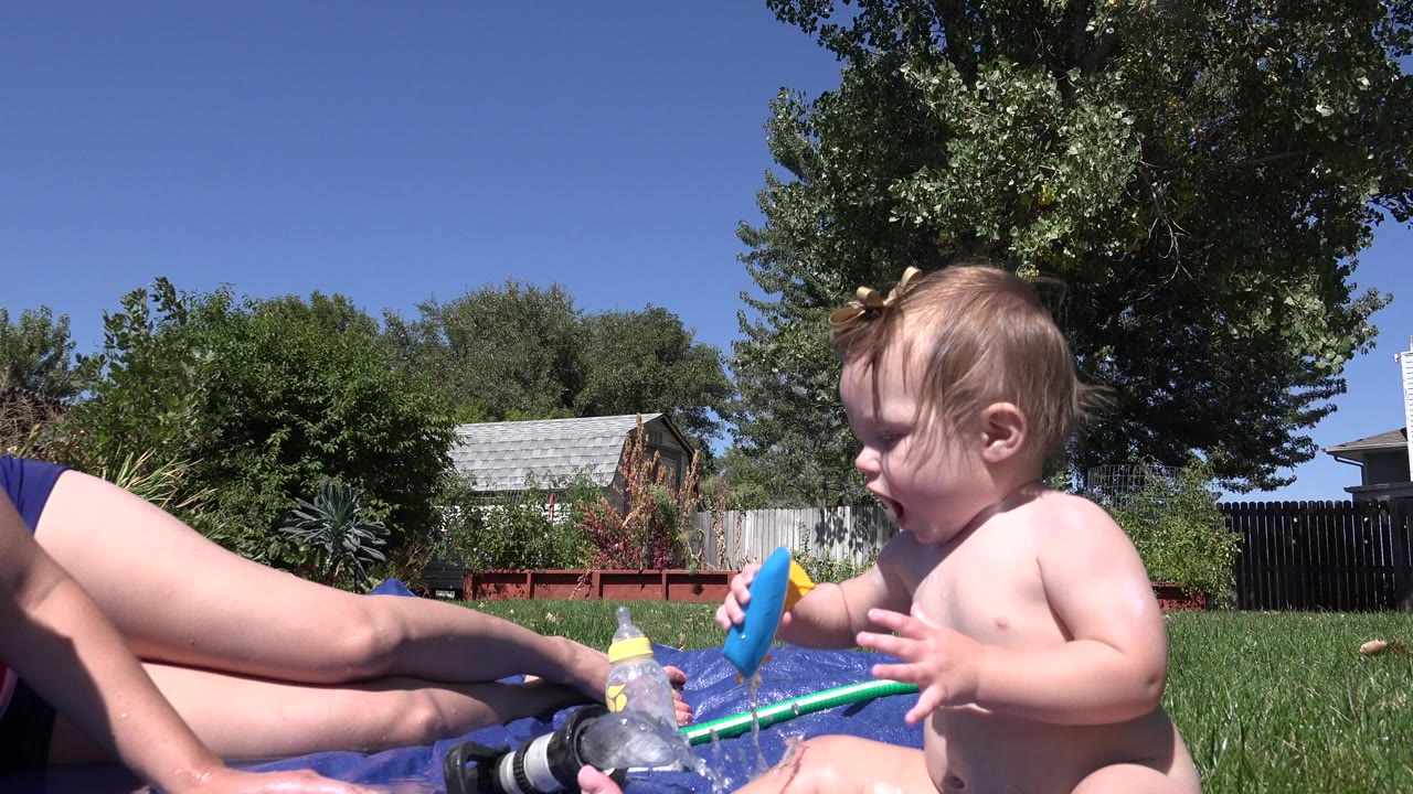 Toddler holding a blue object beside a reclining adult on a sunny lawn.