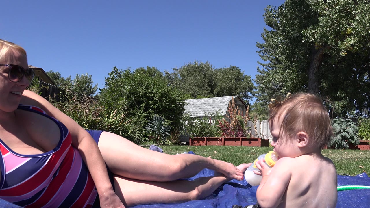 Toddler with bottle beside woman on blue outdoor mat