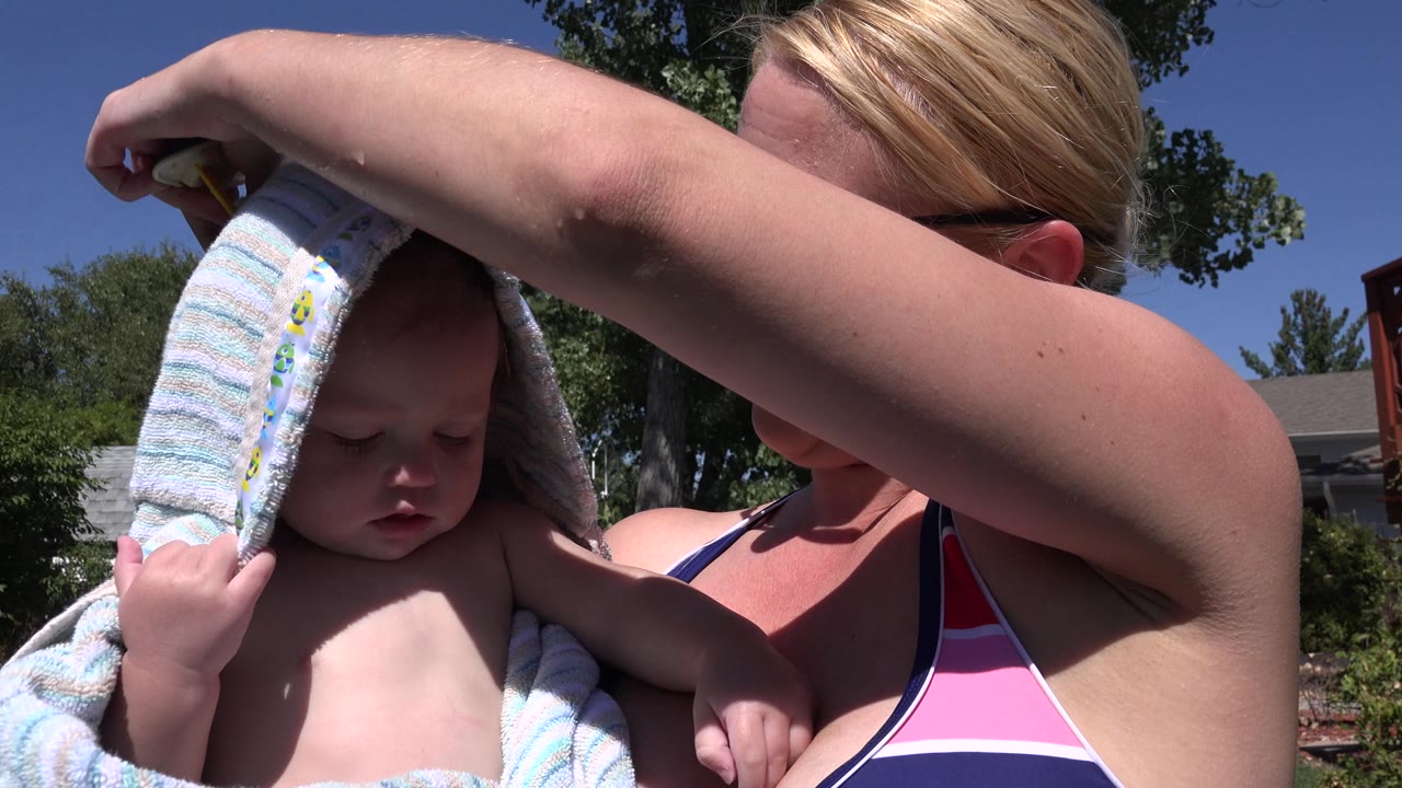 Woman holds a child with the towel pulled back from the child's face.