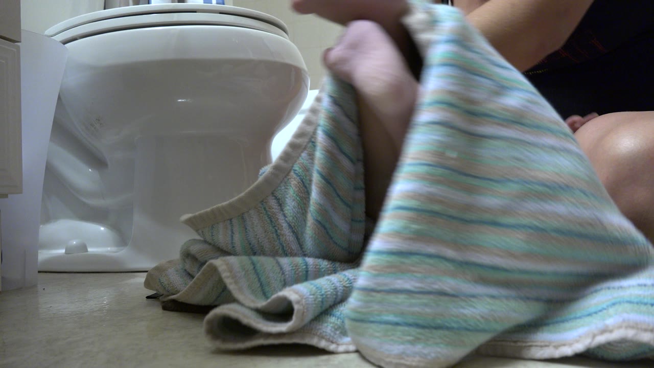 The towel lifts across the foreground beside the toilet as the adult continues drying the young child in a Westminster, Colorado bathroom.