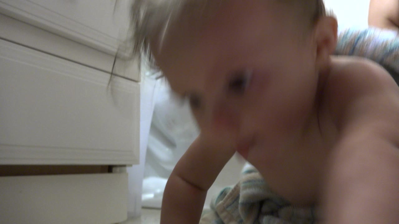 Damp baby crawling close to a bathroom cabinet.