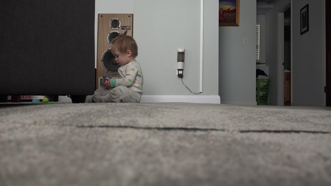 Baby seated by the sofa with a colorful object raised closer to her face.