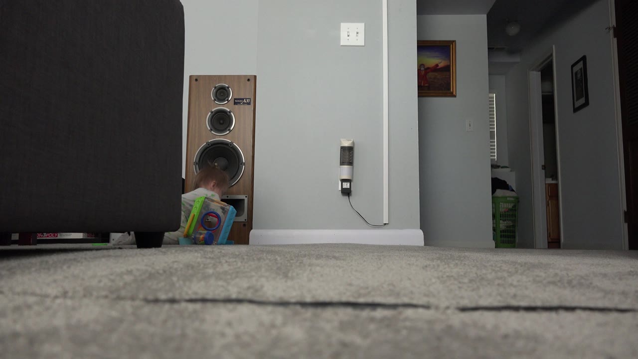 Low view of a living room with a sofa, speaker, toy, and child partly hidden near the floor.