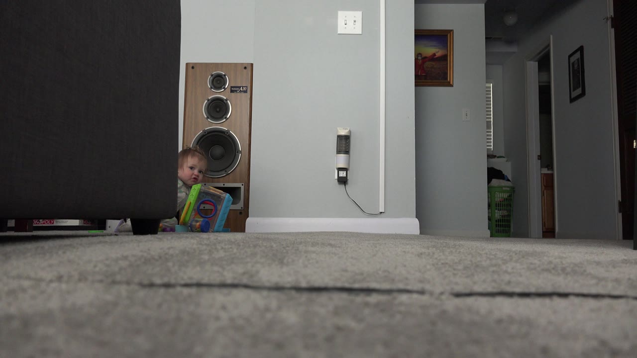 Low carpet view of a child peeking beside a speaker in a living room.
