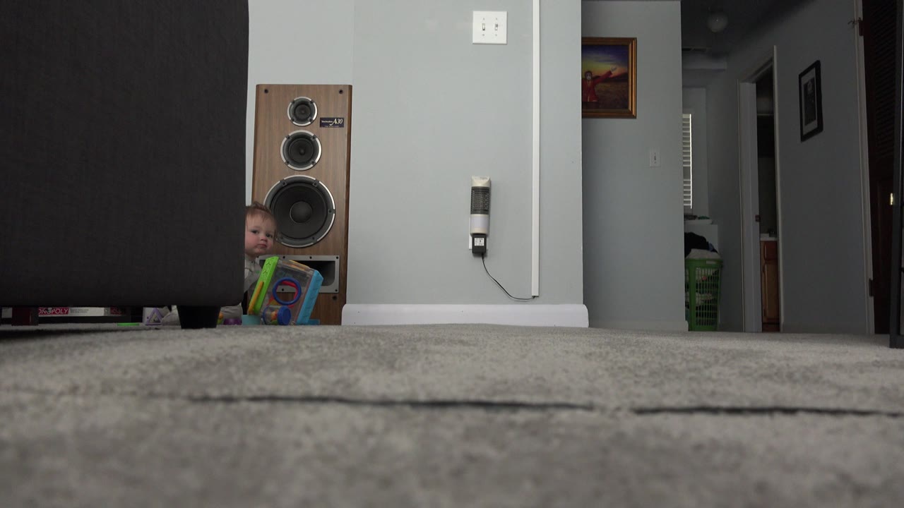 Low carpet-level view of a living room with a speaker and a child partly visible.