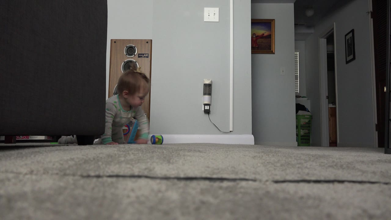 Baby partly hidden beside a dark sofa on a carpeted room floor.