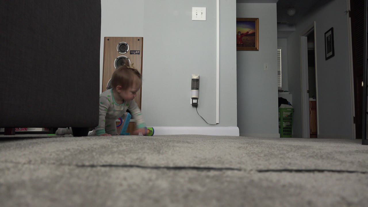 At 0:01 in Westminster, Colorado, the baby is lower beside the sofa with hands near the carpet and a small colorful toy visible in front.