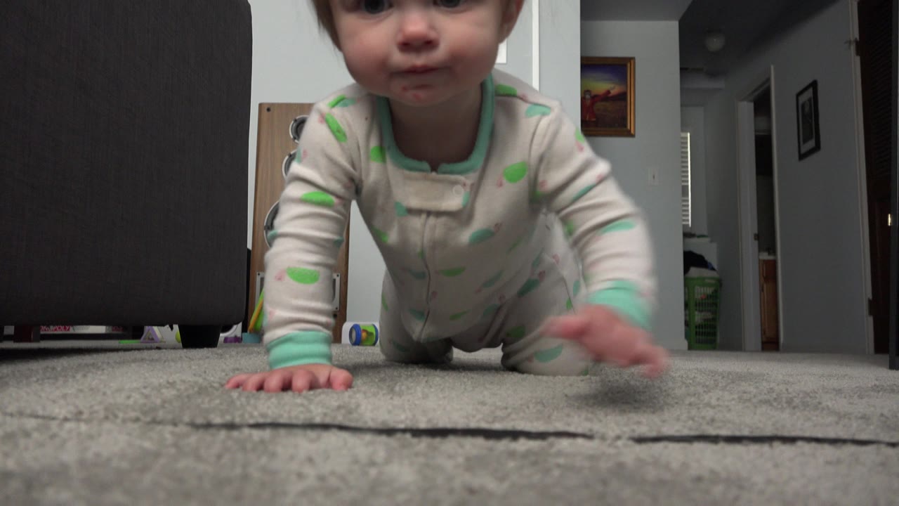 Blonde baby crawling on gray carpet toward a low camera.