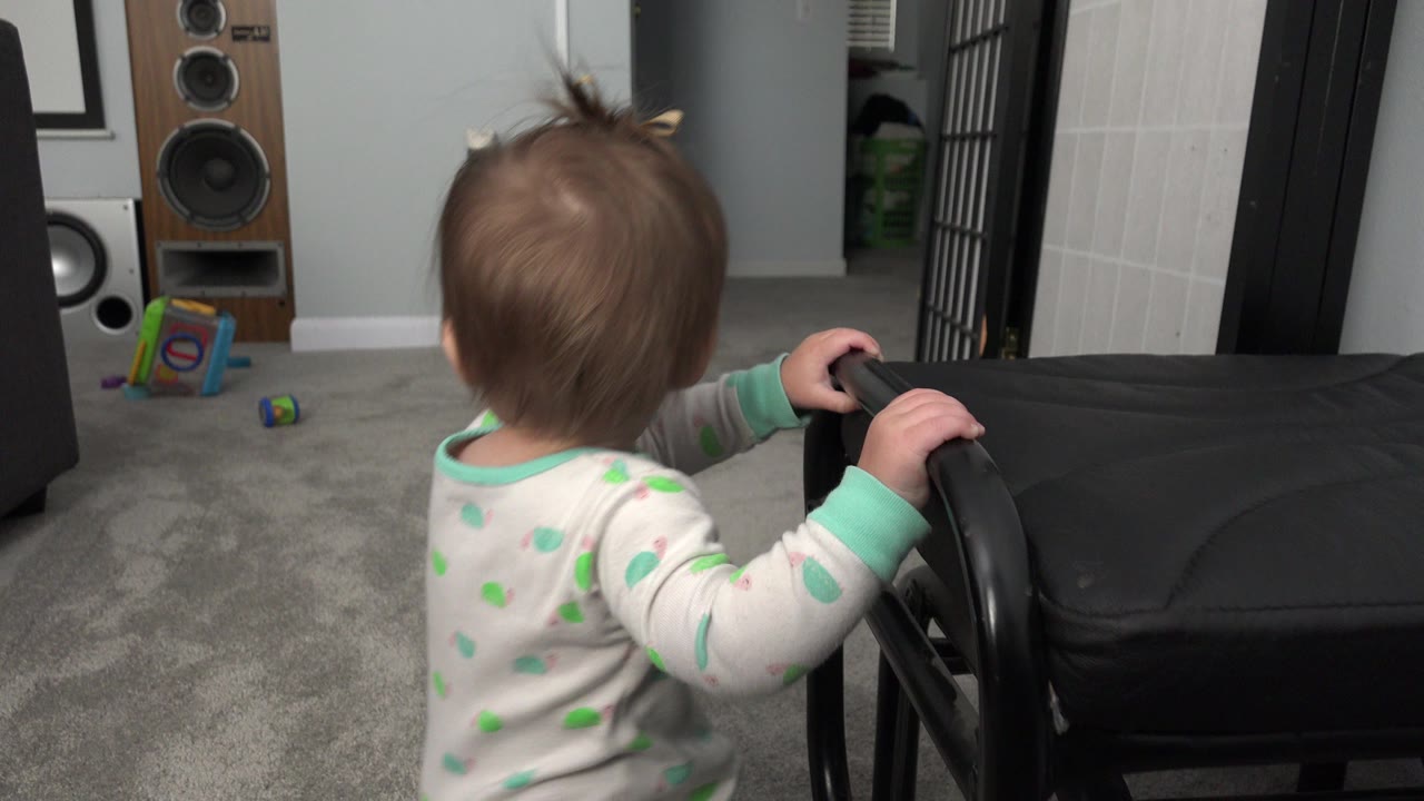 Infant standing near a black chair on gray carpet