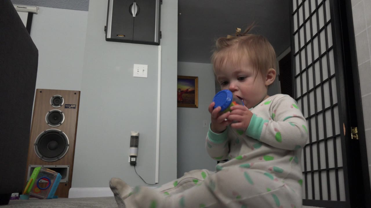 Baby sitting on carpet and holding a blue toy near their mouth.
