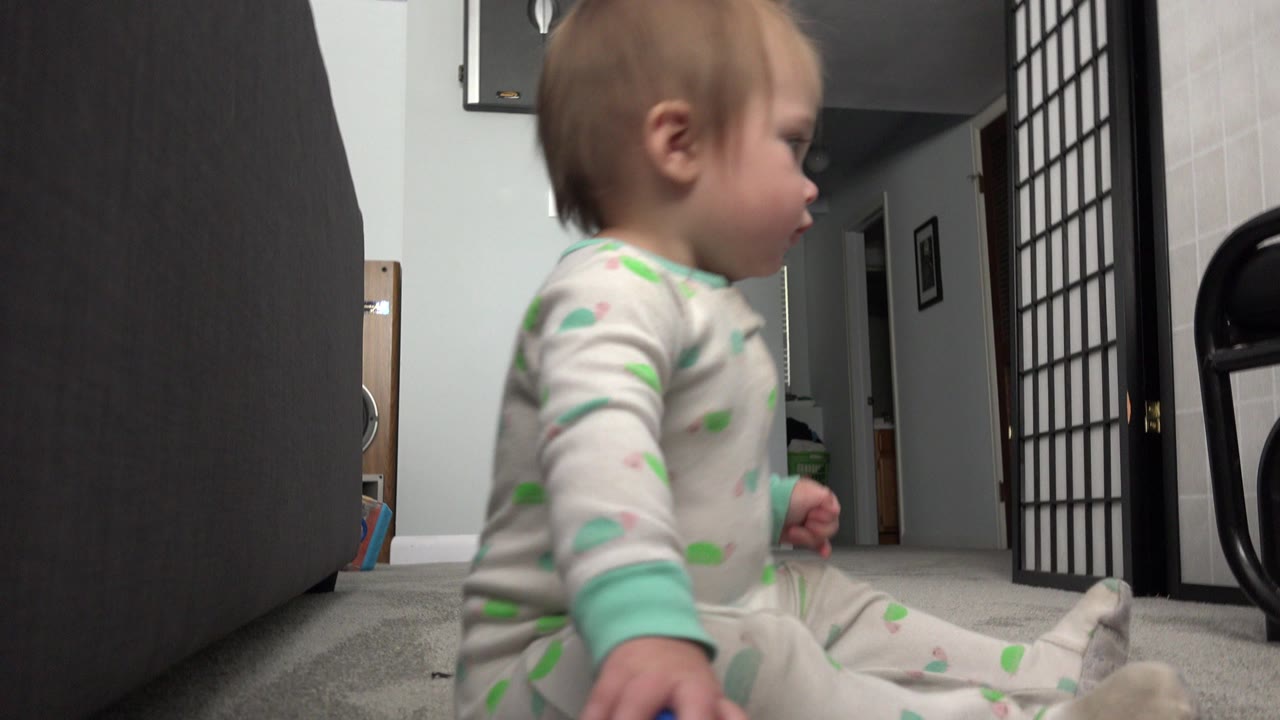 A baby sits in profile on carpet in a Westminster, Colorado home, with dark furniture close to the camera and a folding room divider in the background.