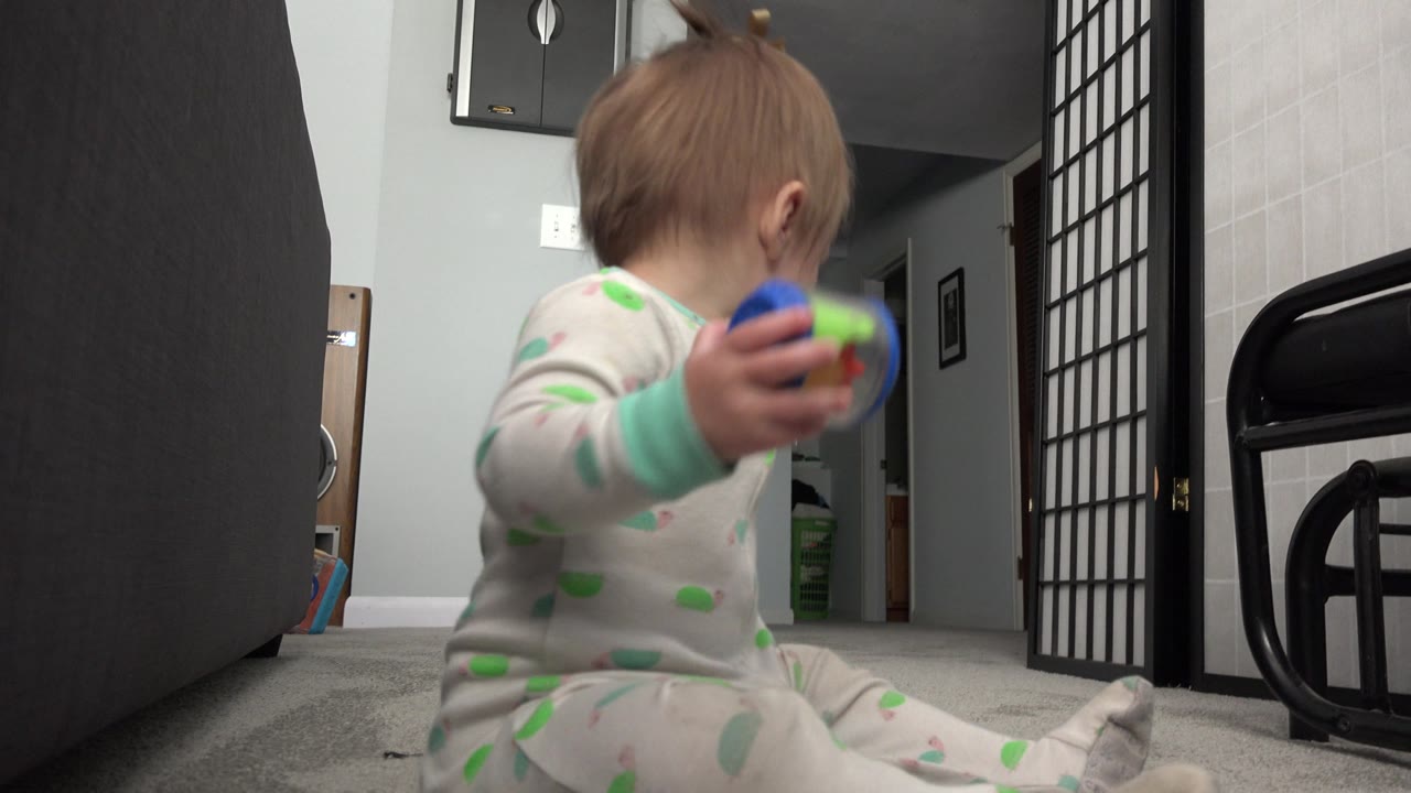 Baby holding a colorful toy while seated on carpet.